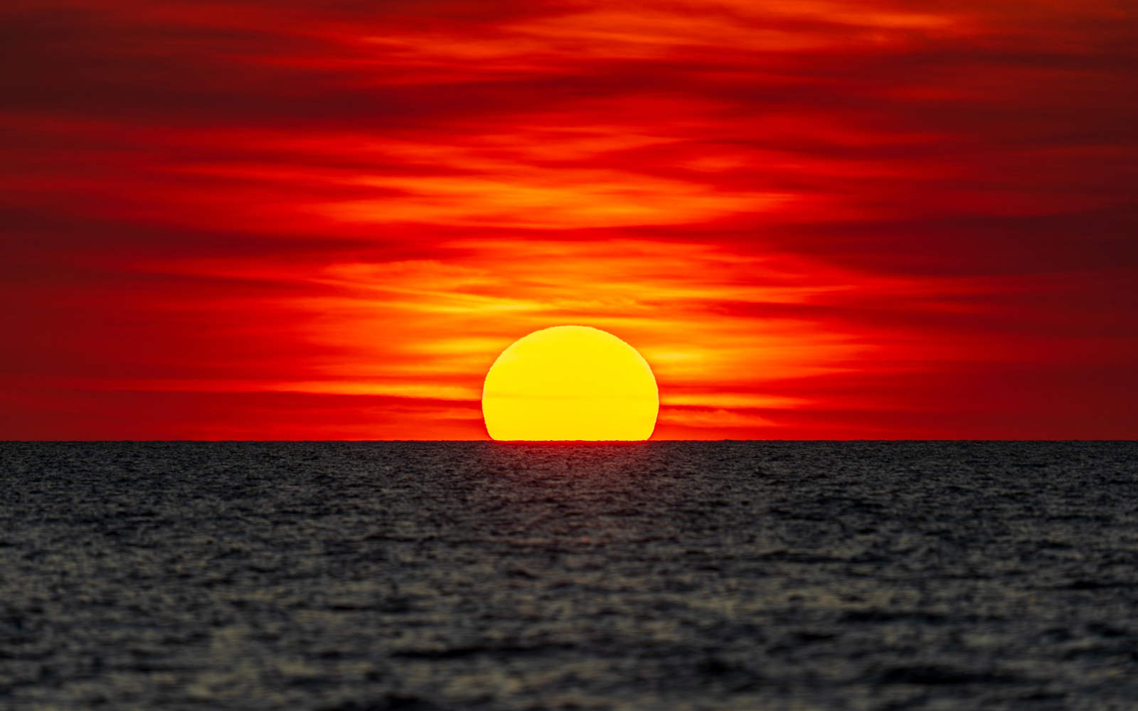 A sunset over water in the colours of the Australian Aboriginal flag